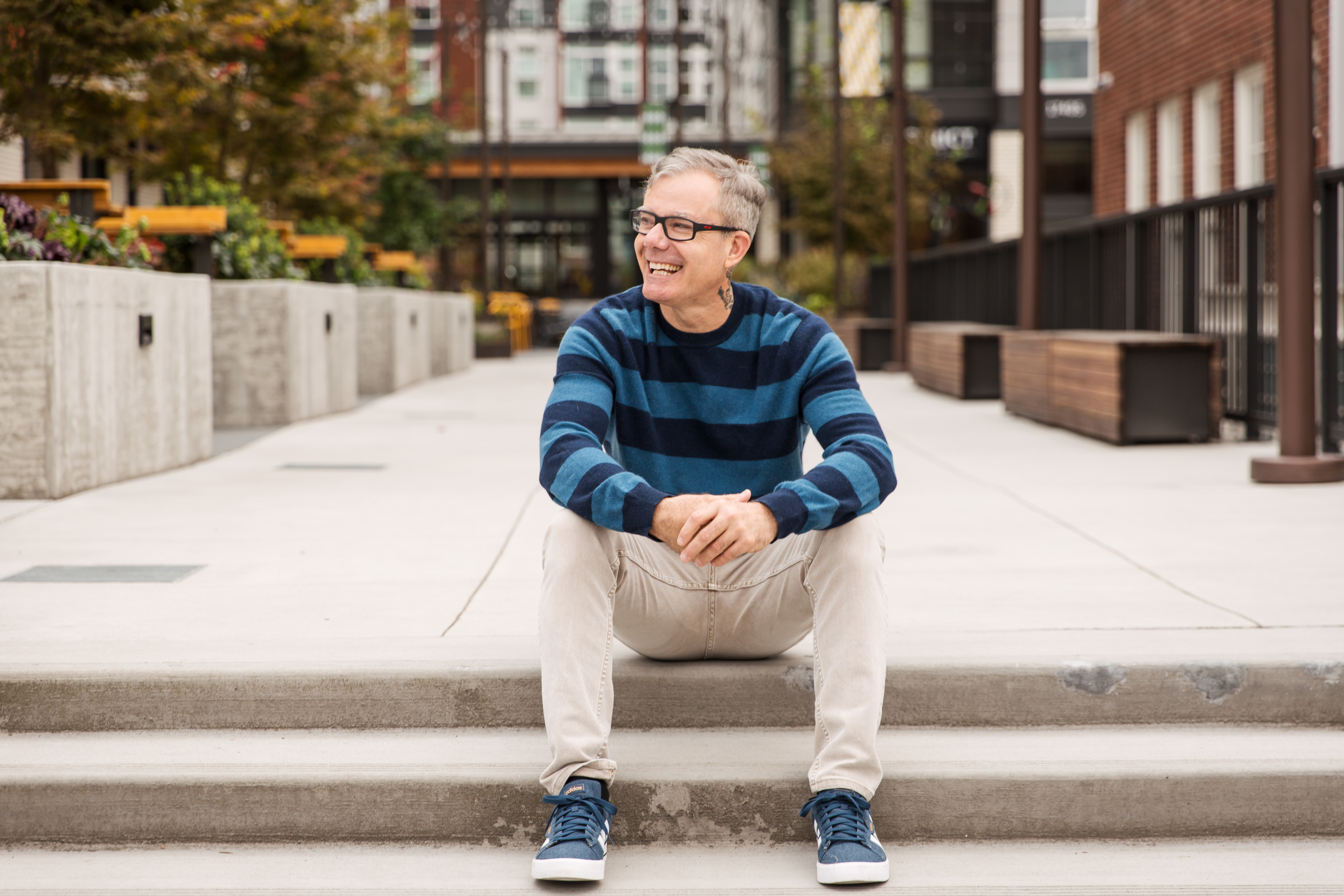 A man in a striped sweater laughing on concrete steps, casual portrait with autumn urban background